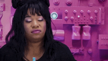 Video gif. A woman is sitting in a pink electrical room and she rolls her eyes.