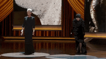 Oscars 2024 gif. We pan across the stage as Rita Moreno, Jamie Lee Curtis, Lupita Nyong'o, and Mary Steenburgen emerge underneath the spotlight. 