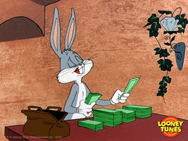 TV gif. Bugs Bunny from Looney Tunes looking very pleased sits at a table, licking his finger so that he can count the giant stack of cash sitting on the table in front of his. Next to him is a large brown bag from which the money came. 