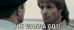 Movie gif. A man angrily says, “Do you wanna go?” and then steps up into another man’s face intimidatingly. He stares down  the other man with wide eyes.