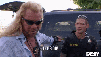 Reality TV gif. Dog the Bounty Hunter is standing with an agent and he looks ready as he nods to the agent and says, "Let's go."
