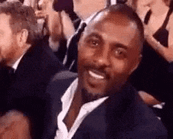 Celebrity gif. Idris Elba is sitting in the audience and he gives us a big thumbs up and a wink before turning to look back at the stage.