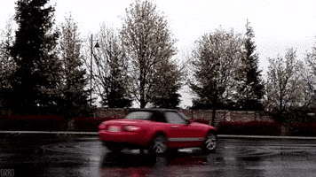 Video gif. A red convertible car does a perfect donut in a parking lot, drifting around in a perfect circle. 