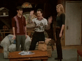 TV gif. A group of friends are standing around when all of a sudden, one friend flips a table over. He flips it in a flippant manner and runs away while the friends exclaim in shock.