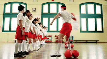 TV gif. Dressed as a coach, Jensen Ackles as Dean on Supernatural hurls a dodgeball at the first kid standing in a line of students.