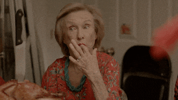 Movie gif. Sitting in front of a cooked turkey with a butcher knife sticking out of it, Cloris Leachman as Josephine on Lez Bomb licks her fingers in enjoyment.