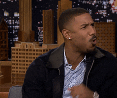Tonight Show gif. Michael B Jordan covers his mouth with his fist and leans back, like someone just got roasted.
