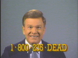 Video gif. Wink Martindale stares at the camera with dead, almost crossed eyes, and a weird smile. The image jitters like an old tv screen, but the man does not move or even blink. On the bottom, the text reads: “1-800-235-DEAD” like it’s an ad for a law practice. 