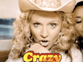 Music video gif. Madonna looks at us straight in the eye with a sultry look before saying, "Crazy," and slowly turns her face down.