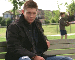 TV gif. Jensen Ackles, as Dean on Supernatural, sits on a park bench and raises a thumbs-up while his mouth creeps into a smile.