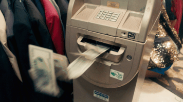 Video gif. Money flies out of an ATM machine. 