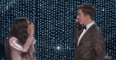 Celebrity gif. Awkwafina and John Mulaney high five and shake hands at the 2019 Academy Awards