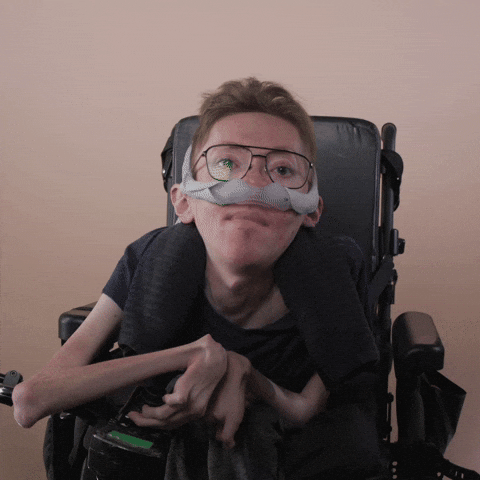 Reaction gif. A mobility-impaired white man using a power chair, a ventilator, and wearing retro-crossbar glasses drifts his eyes closed.