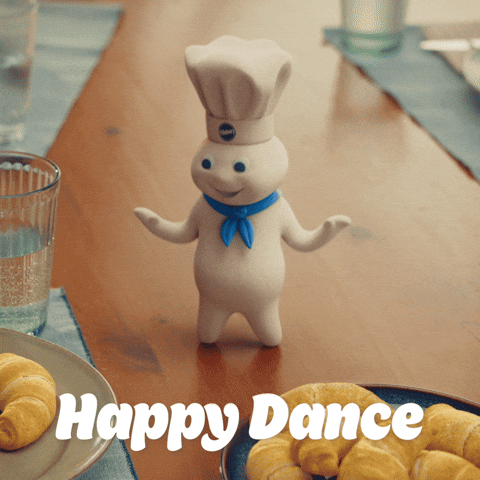 Sponsored gif. The Pillsbury Doughboy, in his iconic blue scarf and Pillsbury chef hat, dances on a holiday table next to a plate of crescent rolls. Text: "Happy Dance" 