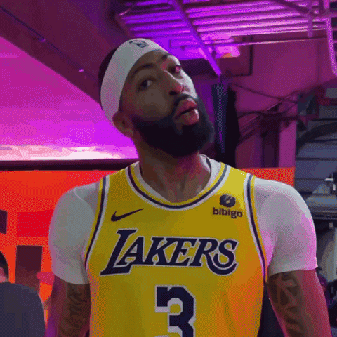 Sports gif. Anthony Davis of the Lakers in a white t-shirt and Lakers jersey walks backstage towards camera, looking at us and breathing out with an exaggerated relieved expression like, "That was a close one." 