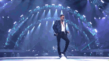 Celebrity gif. Chris Brown wears a black suit and sunglasses as he dances on the American Idol stage with lights beaming in the background.