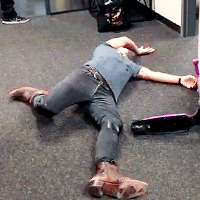 Celebrity gif. Musician Harry Styles lays in a tangled heap on the floor next to an overturned scooter. 