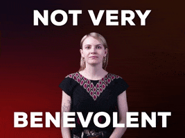 Video gif. Woman leans in and looks at us with an intense side eye, wagging a finger at the camera with a disapproving look against a dark red background. Text, "Not very benevolent." 