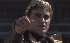 Movie gif. Joaquin Phoenix as Commodus from Gladiator doesn't look happy as he holds out his hand, but gradually looks calmer as he slowly gives us a thumbs up.