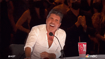 Reality TV gif. Simon Cowell of America's Got Talent clapping and cracking up, leaning back in his chair and rubbing his eyes.
