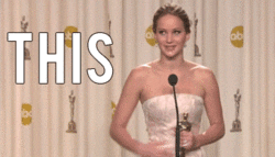 Celebrity gif. Jennifer Lawrence stands in front of a microphone with an Oscar award in her hand. She looks around with big eyes and gestures her arms out, then slapping her side. Text, “This.”