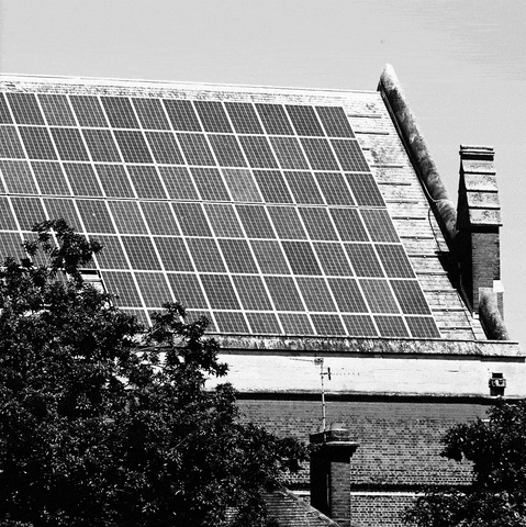 Text gif. Sticker in the style of Barbara Kruger, red with white oblique Futura lettering, reading "Go solar," slaps across a black-and-white photo of a post-medieval English-style urban house with solar panels on the roof.