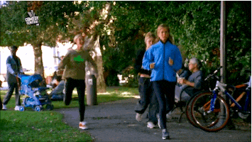 TV gif. In a lively park, a woman with short braids runs noisily past the other joggers.