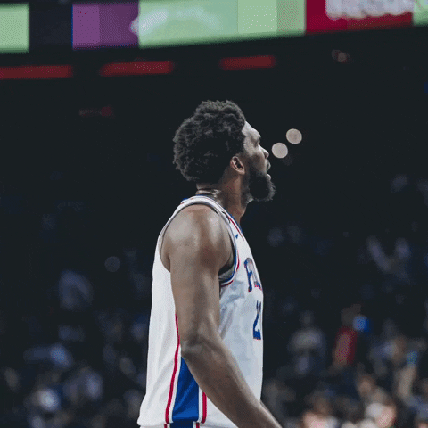 Sports gif. Joel Embiid from the Philadelphia 76ers is on the court and he's hyped up. He looks at the crowd and points down at the court, rallying them.