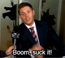 Celebrity gif. Jensen Ackles is being interviewed and he throws a hand to the side before grinning and saying, "Boom! Suck it!"
