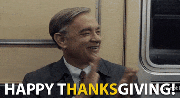 Movie gif. Sitting in a subway seat, Tom Hanks as Mr. Rogers in A Beautiful Day in the Neighborhood smiles and claps his hands. Text, "Happy Thanksgiving!" In the text, "Hanks" is highlighted yellow.