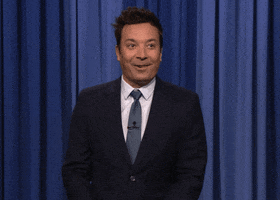 The Tonight show gif. Jimmy Fallon looks at the audience and then at us as he bites his lip and pumps his fist in celebration