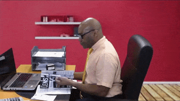 Video gif. Exasperated man sitting at an office desk flips a pamphlet closed, tosses all the papers off his desk, then leans back in his chair and crosses his arms.