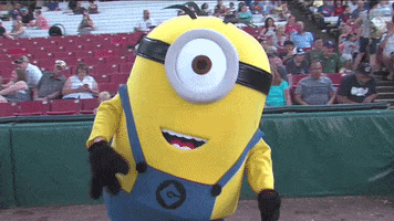 Sports gif. A person in a giant Minions mascot costume dances for us on the field as a baseball game, its arms flailing out to the side.