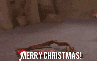 Cartoon gif. In a scene from Rudolph the Red-Nosed Reindeer, a stop-motion Rudolph picks up a set of jingly reins from the floor with his nose and proudly puts them on, but he's not exactly wearing them right. The text "Merry Christmas!" is wearing a Santa hat.
