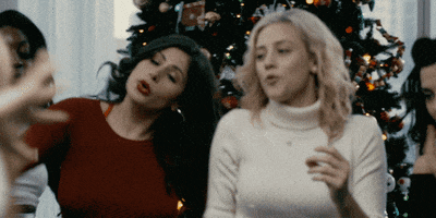 Movie gif. Lili Reinhart as Annabelle in Hustlers dancing in front of a Christmas tree with other women dancing.