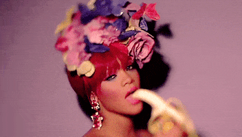 Celebrity gif. Sexy Rihanna looks at us seductively as she slowly puts a peeled banana in her mouth.