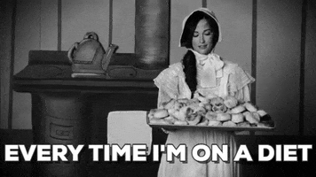 Music video gif. From the video for Biscuits, black-and-white vintage-style clip of Kacey Musgraves wearing a bonnet and prairie dress, holding a pan piled high with biscuits.