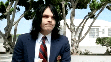 Music video gif. Gerard Way of My Chemical Romance in the I’m Not Okay (I Promise) music video wears a preppy school uniform and shakes his head with a disappointed expression on his face.