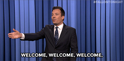 Tonight Show gif. Jimmy Fallon as host stands in front of blue velvet stage curtains and faces his audience. He extends a hand in greeting, and turns to greet each section in turn saying "welcome" to each. Text. Welcome, welcome, welcome, welcome, welcome, welcome, welcome.