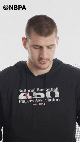 Video gif. Nikola Jokic of the Denver Nuggets shoots us a frowny face, eyebrows raised like he's pleading with us and making a puppy dog face. The NBPA logo appears in the top corner.
