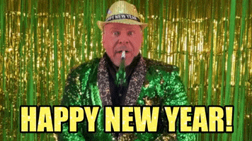 Holiday gif. In front of a bright green and gold tinsel curtain, a man dressed in an emerald green sequined suit blows into a matching colored party blower. He wears a blingy gold hat that reads, "Happy New Year," which also reads as text at the bottom.
