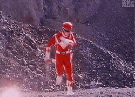 TV gif. The Red Ranger from Mighty Morphin Power Rangers frantically flails his arms as he runs toward us through sparking explosions in a rocky battlefield.