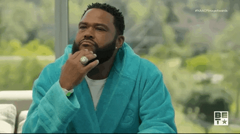 Celebrity gif. Anthony Anderson sits in a teal robe with a giant ring on his finger. His hand is on his face in a thinking pose, his eyes narrowed.