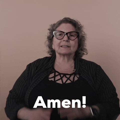 Reaction gif. A Disabled white woman with kinky curly gray hair and big wine-colored cat-eye glasses hands pressed together in prayer, makes a show of saying, "Amen!"