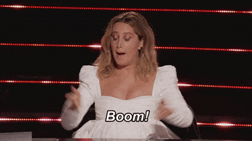 Reality TV gif. In a clip from The Masked Dancer, Ashley Tisdale wears a white dress as she holds up her pointer fingers and exclaims: Text, "Boom!"
