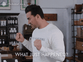 Schitt's Creek gif. Dan Levy as David in a salon, pointing to a product bottle appearing uncomfortable and turning back around as he says, "What just happened?"