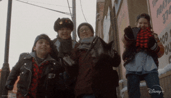 Disney gif. Four boys in The Mighty Ducks: Game Changers give each other five and celebrate as they stand together in winter gear on a city street.