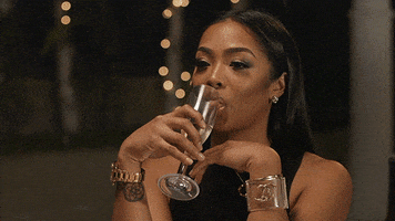 Reality TV gif. A woman takes a sip of champagne before tossing it across the table into her dinner companion's face.