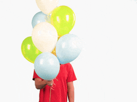Celebrity gif. Austin Mahone is holding a bunch of balloons and hides behind it. He pops out from behind and gives us a bashful smile and wave.