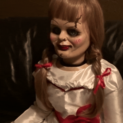 Movie gif. The blonde pig-tailed Annabelle doll from Annabelle slowly turns its scarred and bloody face. 